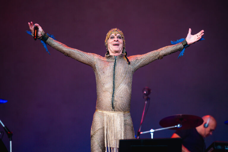 The Town celebra Ney Matogrosso em performance icônica no palco The One; artista brasileiro surge com figurino dourado, braços abertos e expressão de êxtase, encantando o público com sua presença cênica marcante.
