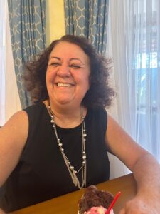 Mulher sorridente aprecia sobremesa em ambiente interno com decoração elegante de cortinas e móveis de madeira.