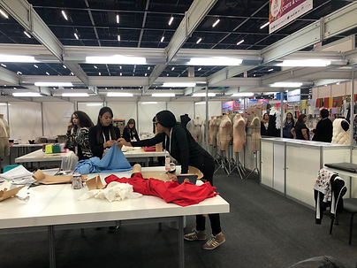 Desafio de Moda na Mega artesanal 2025 apresenta participantes costurando e preparando peças de roupa em ambiente de exposição.