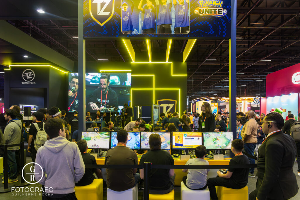 Tuzzy promove partidas de Pokémon Unite na Gamescom Latam 2025 com visitantes jogando em monitores.