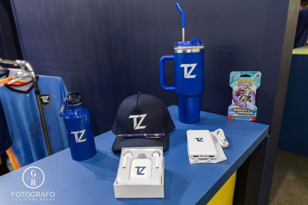 Tuzzy exibe brindes como copo térmico, boné, fone, garrafa, powerbank e carta Pokémon.