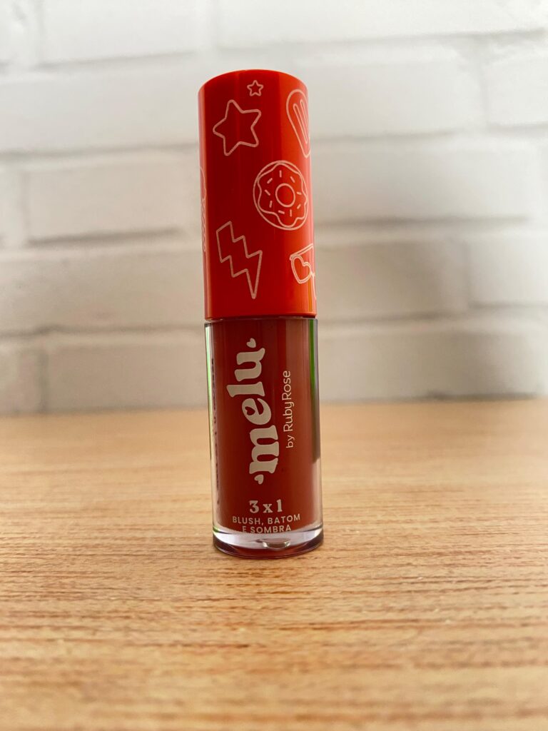 Blush multifuncional Ruby Rose da linha Melu com fórmula 3 em 1 para ser usada como batom, blush e sombra. Embalagem cilíndrica vermelha com tampa ilustrada em tons laranja.