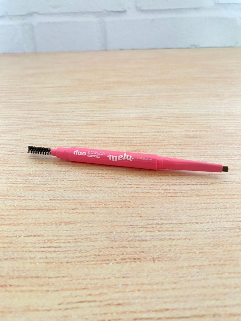 Lápis 2 em 1 Ruby Rose da linha Melu, com ponta retrátil de um lado e escovinha do outro. Ideal para preencher e pentear as sobrancelhas com praticidade.