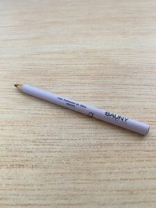 Bauny lápis delineador de olhos na cor marrom, com corpo lilás claro e tampa transparente. O produto tem visual minimalista e acabamento fosco.