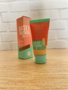 Vizzela base líquida vegana com bisnaga laranja e verde, texto em branco e tampa verde. Ao lado, a caixinha repete o design com destaque para “cruelty free & paraben free”.