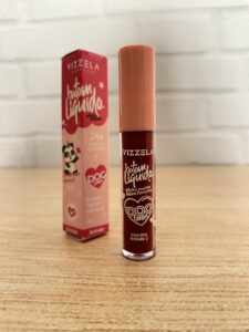 Vizzela batom líquido com efeito matte ultra fixação, em embalagem cilíndrica com tampa rosa clara e corpo transparente que revela a cor vinho intensa. Ao fundo, caixa rosa e coral decorada com panda e a frase “DOG Lovers”.