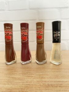 Dailus reúne quatro esmaltes com embalagens temáticas: três da linha Choco Cherry nas cores marrom escuro, vinho e marrom claro, e um com glitter dourado da coleção Babado e Glitteria, com tampa preta.