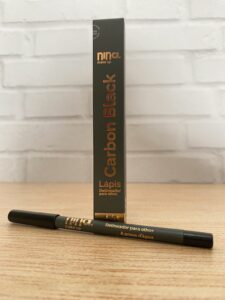 Nina MakeUp lápis delineador preto “Carbon Black”, com corpo grafite, tampa preta e escrita dourada. Acompanha embalagem vertical com o mesmo padrão de cor. Indicado como à prova d’água.