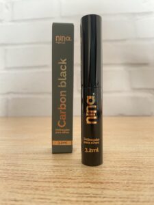 Nina MakeUp delineador líquido preto com embalagem cilíndrica preta e detalhes dourados, ao lado da caixinha grafite com o nome “Carbon Black” em destaque. Contém 3,2 ml.