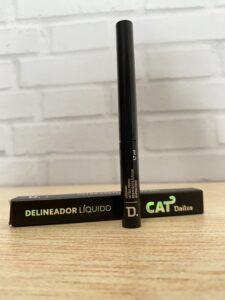 Dailus delineador líquido preto em embalagem fina e cilíndrica com acabamento fosco, acompanhado da caixa preta com o nome “CAT Dailus” em verde e branco.