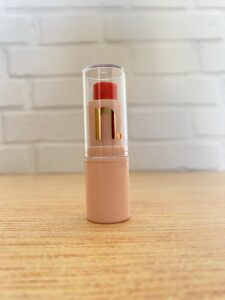 Nina MakeUp balm labial vermelho em bastão, com embalagem nude e tampa transparente, exibindo logo dourado “n.” sobre fundo branco.