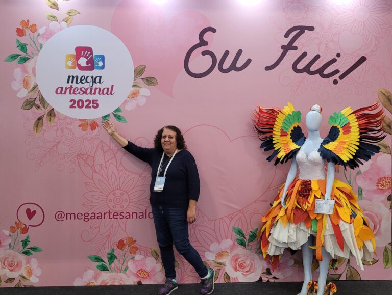 Mega Artesanal 2025 registra momento especial de visita ao painel “Eu Fui!”, com cenário decorativo e manequim vestindo figurino artístico feito em papel colorido, destacando o clima acolhedor e inspirador da feira.