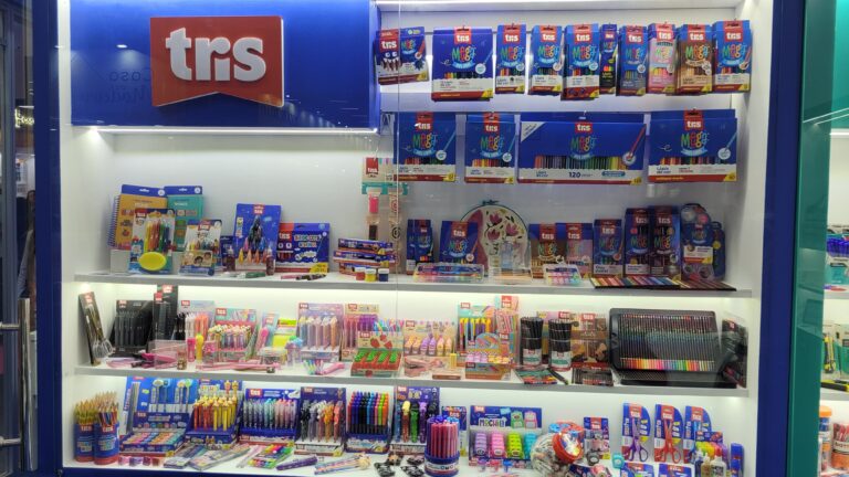 Tris apresenta vitrine colorida com ampla variedade de produtos escolares e de papelaria, incluindo lápis de cor, canetas, marcadores, apontadores, colas e kits criativos da linha Megapack expostos na Mega Artesanal 2025.