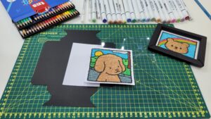 Tris demonstra o uso de lápis de cor e marcadores artísticos em oficina criativa com desenhos de animais aplicados em cartões personalizados, destacando a aplicação prática de seus produtos para arte e artesanato.