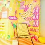 Espaço temático da linha Banana da Melu com cenografia tropical e cadeira de praia na Beauty Fair 2025.