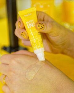 Hidratante labial da linha Banana da Melu sendo aplicado na pele durante a Beauty Fair 2025.