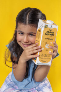 Criança sorridente segurando embalagem da bebida vegetal Completo da A Tal da Castanha, produto rico em proteína, cálcio e fibras.
