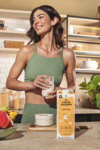 Mulher em estilo de vida saudável preparando café da manhã com bebida vegetal Completo da A Tal da Castanha na cozinha.