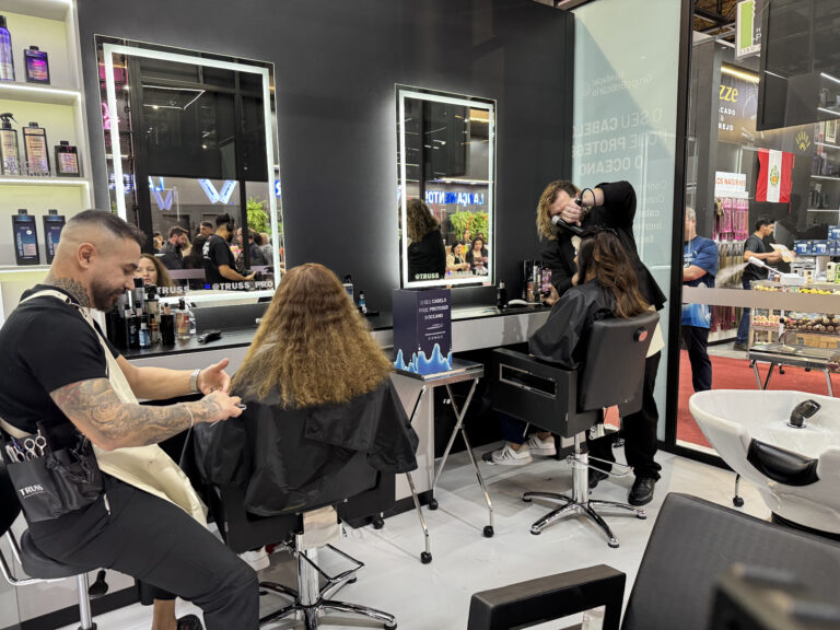 Profissionais realizam cortes de cabelo no estande da Fundação Grupo Boticário na Beauty Fair 2025, incentivando doações de fios para projetos ambientais.