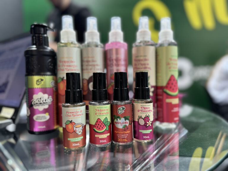 Frascos da linha Tentação Kamaleao expostos na Beauty Fair, com perfumes capilares e body splash em fragrâncias como pitaia e baunilha.
