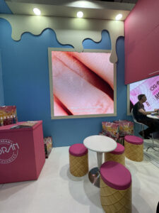 Área de convivência no estande da Poran na Beauty Fair 2025, com puffs em formato de casquinha de sorvete e comunicação visual temática.