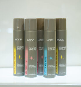 Perfume Capilar Mood em versões Yellow Glow, Glow Up e Deep Glow, com foco em cabelos perfumados e brilhantes, expostos em prateleira iluminada.