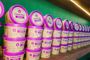 Linha Purple Mask da Lola Cosmetics exposta na feira, máscaras reparadoras para cabelos loiros e com mechas em embalagens lilás e branca.