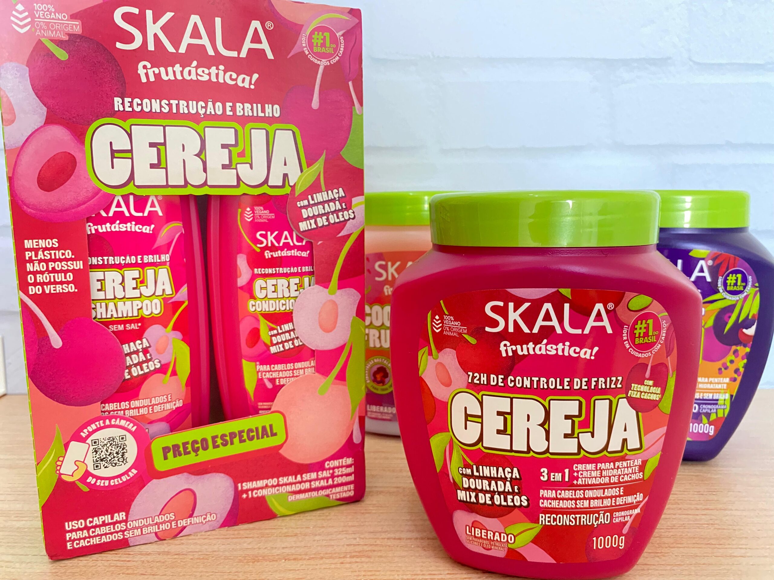 Kit Skala Frutástica Cereja com shampoo, condicionador e máscara de reconstrução e brilho expostos sobre mesa de madeira.