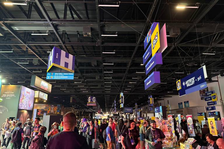 Público circula pelos corredores movimentados da CCXP, com estandes coloridos, placas suspensas e artistas expondo suas obras no Artist’s Valley em São Paulo.