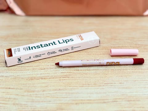 Lápis labial Instant Lips Nina MakeUp sobre mesa, com embalagem em tons de rosa e tampa removida mostrando a ponta vermelha.