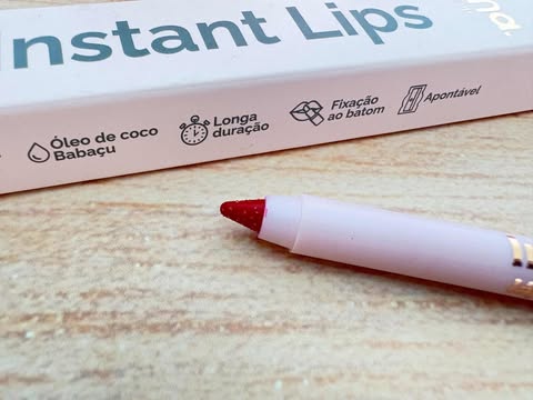 Close do lápis Instant Lips Nina MakeUp mostrando textura, ponta apontada e rótulo com ícones de longa duração e óleo de babaçu.