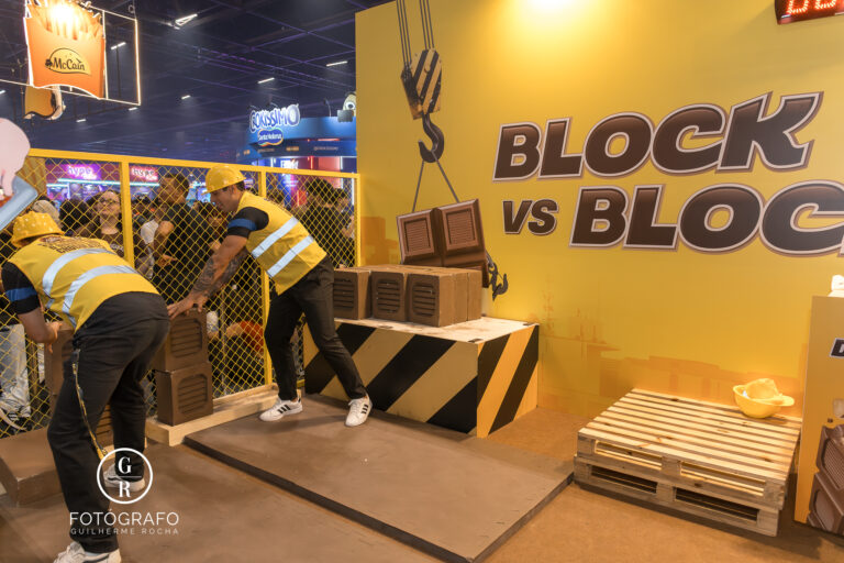 Visitantes competem na brincadeira Block vs Block do estande da Arcor na BGS 2025, empilhando blocos de chocolate em um desafio divertido e físico.