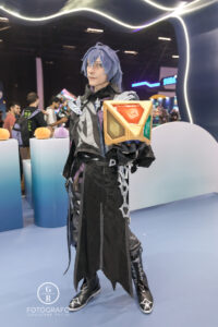 Cosplayer de Genshin Impact exibe um cubo elemental colorido no estande do jogo durante a BGS 2025, representando os poderes do universo de Teyvat.