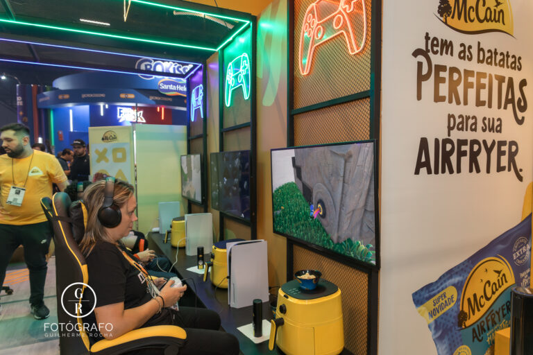 Estande da McCain na BGS 2025 com visitantes jogando em consoles PlayStation ao lado de Air Fryers, destacando o conceito de praticidade e batatas prontas em dez minutos.