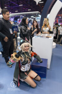 Cosplayer caracterizada como personagem de Genshin Impact posa sorridente ao lado da área de ativações do estande na BGS 2025, interagindo com o público.