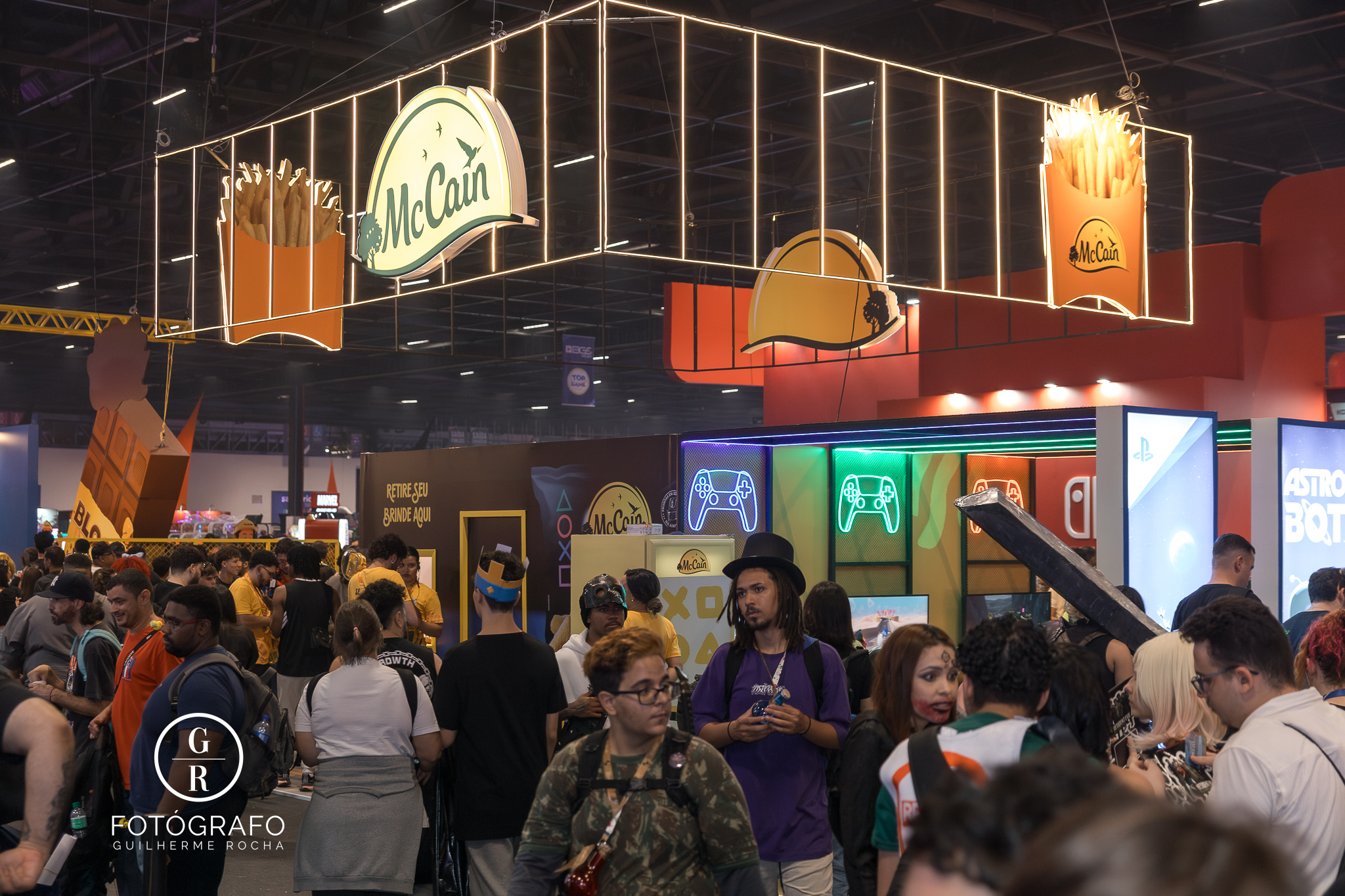 Estande da McCain na BGS 2025 com decoração temática da PlayStation, expositores com luzes coloridas, consoles para demonstração e grande público participando das ativações.