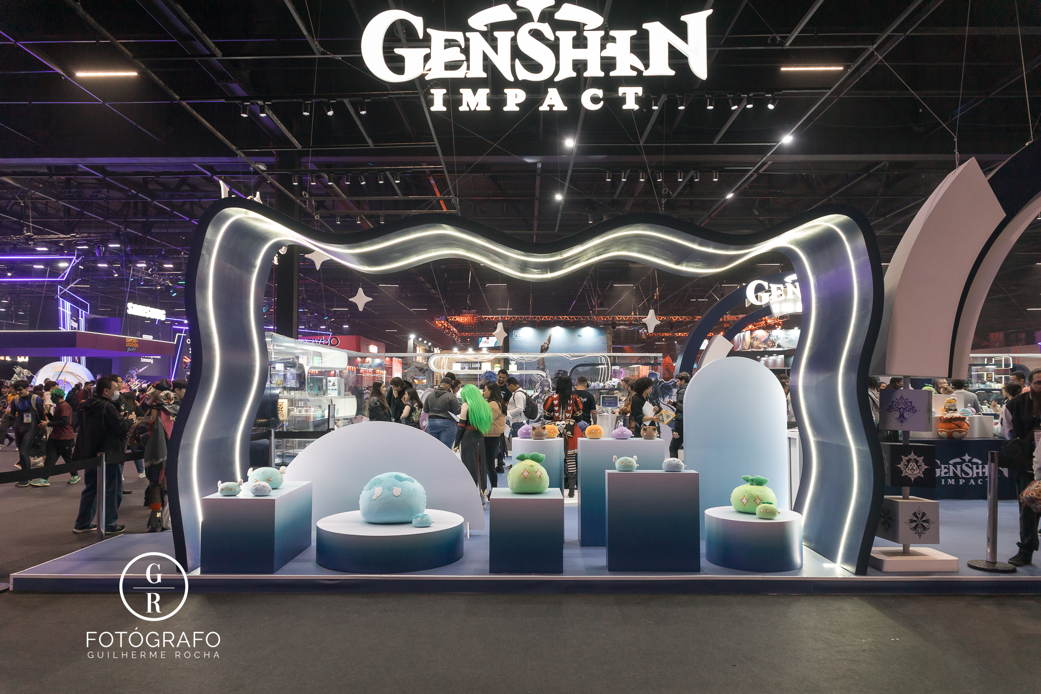 Estande de Genshin Impact na BGS 2025 com pelúcias de Slimes, iluminação temática e design inspirado no universo do jogo, atraindo grande público durante o evento.