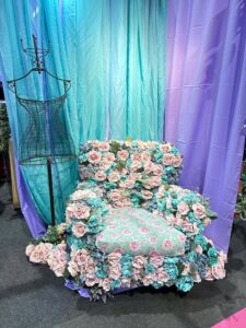 Cenário instagramável da Criativa com poltrona decorada com flores cor-de-rosa e azul, cortinas coloridas e manequim de ferro.