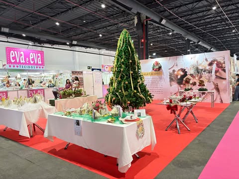 Exposição de Natal na Criativa Campinas 2025 com uma grande árvore decorada ao centro, mesas temáticas com peças artesanais e cenário festivo dentro do pavilhão do evento.