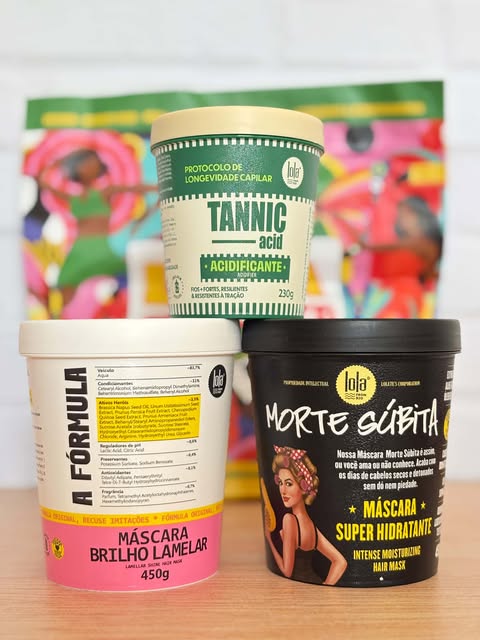 Três máscaras capilares Lola — Tannic Acid, Morte Súbita e Brilho Lamelar — empilhadas sobre uma mesa com embalagens vibrantes.