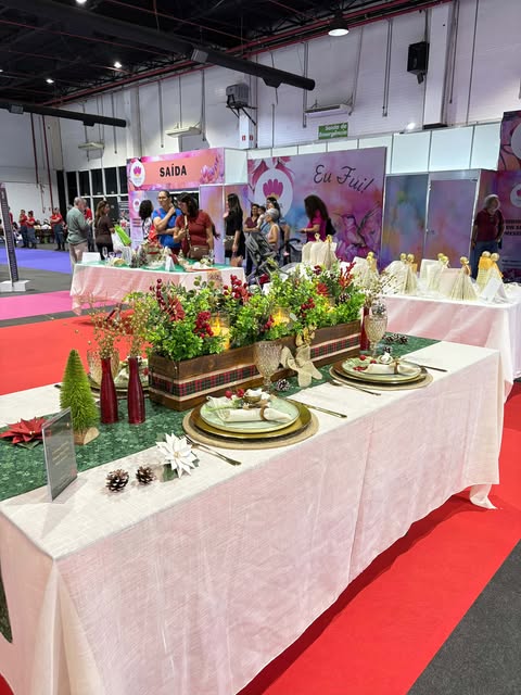 Mesa decorada com tema natalino na Criativa Campinas, com enfeites artesanais, arranjos coloridos e detalhes festivos sobre toalha branca.