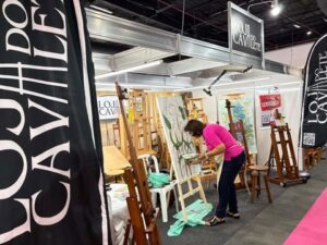Estande da Loja do Cavalete na Criativa, com exposição de cavaletes e pintura ao vivo realizada por uma artista.
