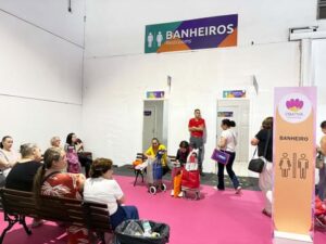 Espaço dos banheiros na Criativa, com bancos para descanso e visitantes aguardando em um corredor sinalizado em rosa.
