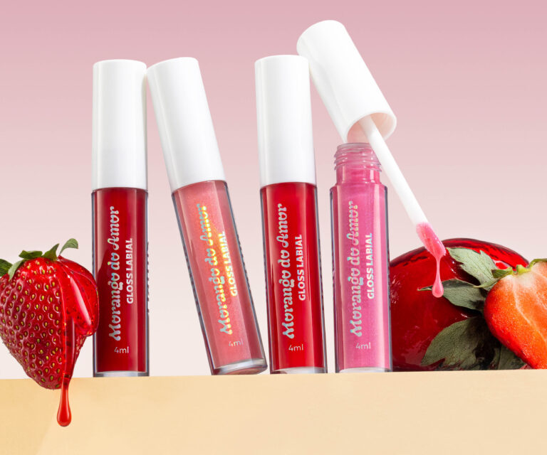 Glosses Morango do Amor da Dailus alinhados em close, com morango e calda vermelha escorrendo em fundo rosa, destacando brilho e textura translúcida.