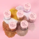 Ecobrilhos Vizzela para o natal, com diferentes tons cintilantes em potes rosados, dispostos sobre fundo rosa.