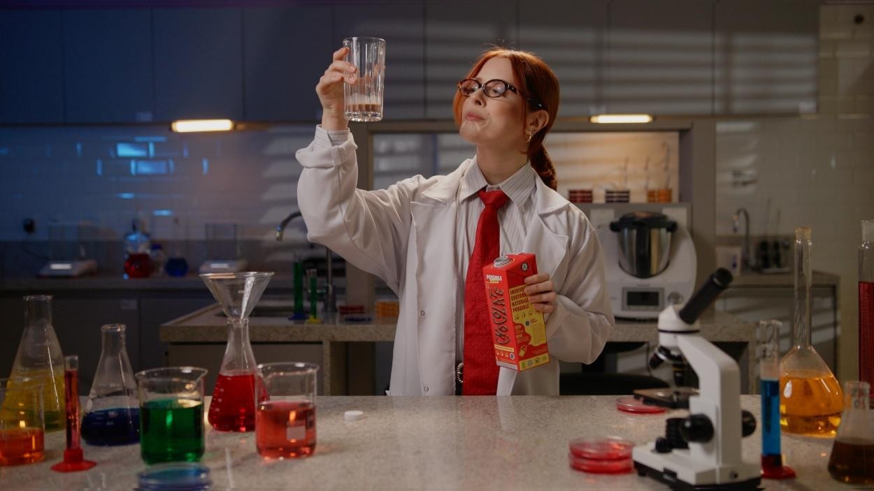Cientista em laboratório analisa bebida vegetal Possible, segurando embalagem de achocolatado enquanto observa amostras coloridas em um cenário científico.