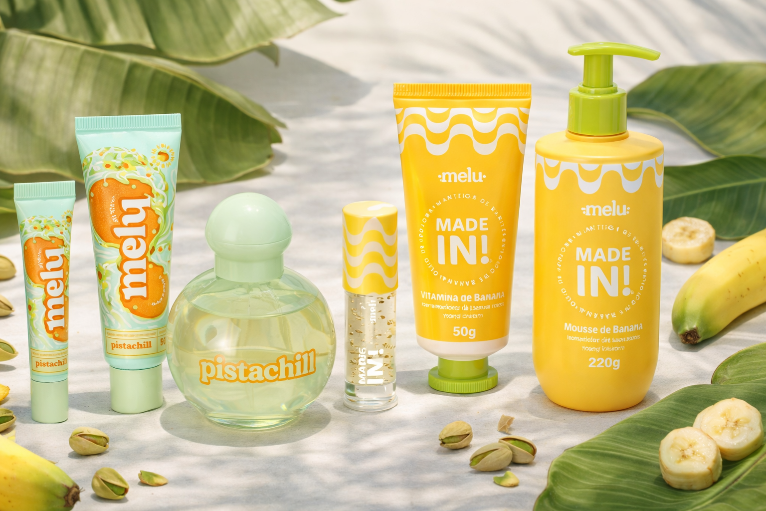Linha melu Made In e Pistachill com hidratantes, lip oil, desodorante colônia e mousse de banana, dispostos sobre superfície clara com folhas tropicais, bananas e pistaches decorativos ao redor.