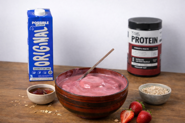 Smoothie bowl de morango cremoso servido em bowl, acompanhado de bebida vegetal Possible Original, proteína vegetal, aveia, mel e morangos frescos sobre a mesa.