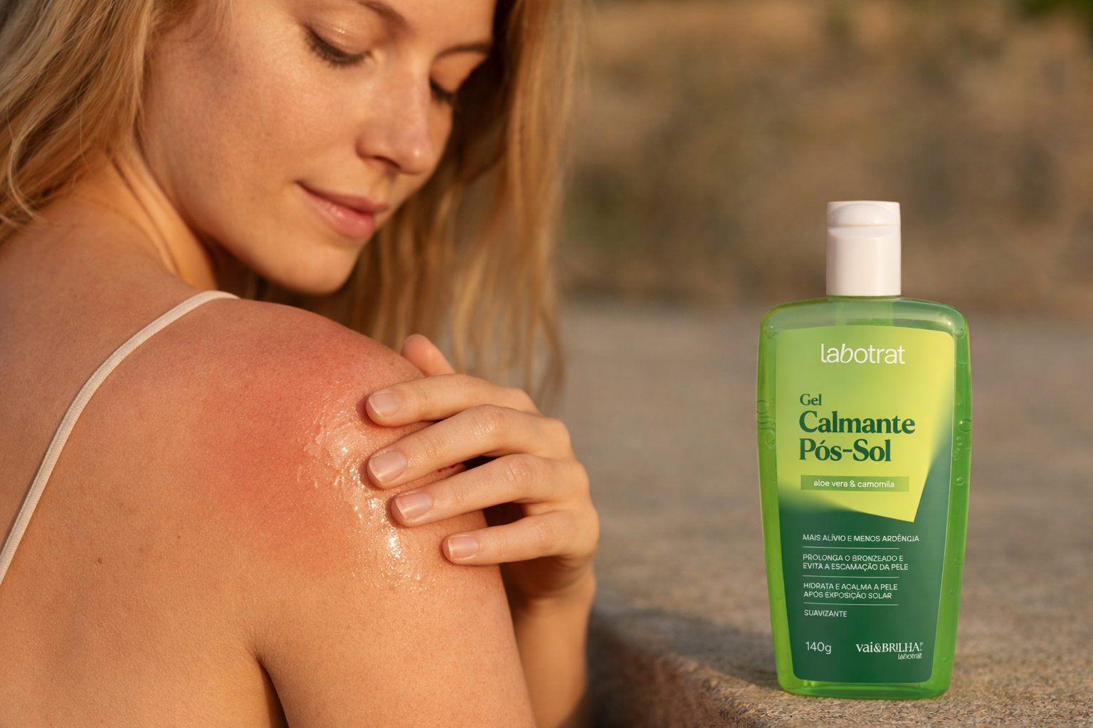 Mulher loira aplicando o Gel Calmante Pós-Sol labotrat em ombro levemente avermelhado pelo sol, em cenário externo com luz dourada natural e produto posicionado ao lado.