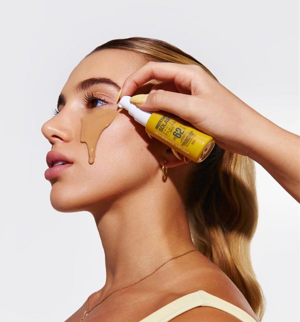 Close de aplicação do protetor solar facial fluido PINK CHEEKS com textura leve sendo espalhada na pele do rosto
